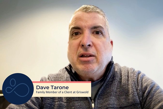 A man with short gray hair and a beard speaks in an indoor setting. The text on the image reads "Dave Tarone, Family Member of a Client at Griswold In-Home Care Services.