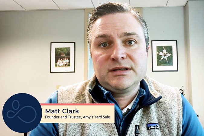 A man in a fleece vest looks at the camera. A nameplate at the bottom reads "Matt Clark, Founder and Trustee, Amy's Yard Sale." There are framed pictures on the wall behind him, hinting at his experience in providing elderly care assistance.