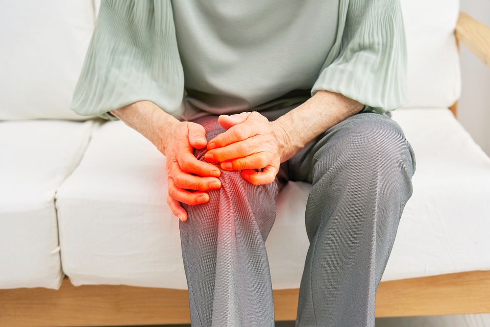 An elderly person gripping their right knee