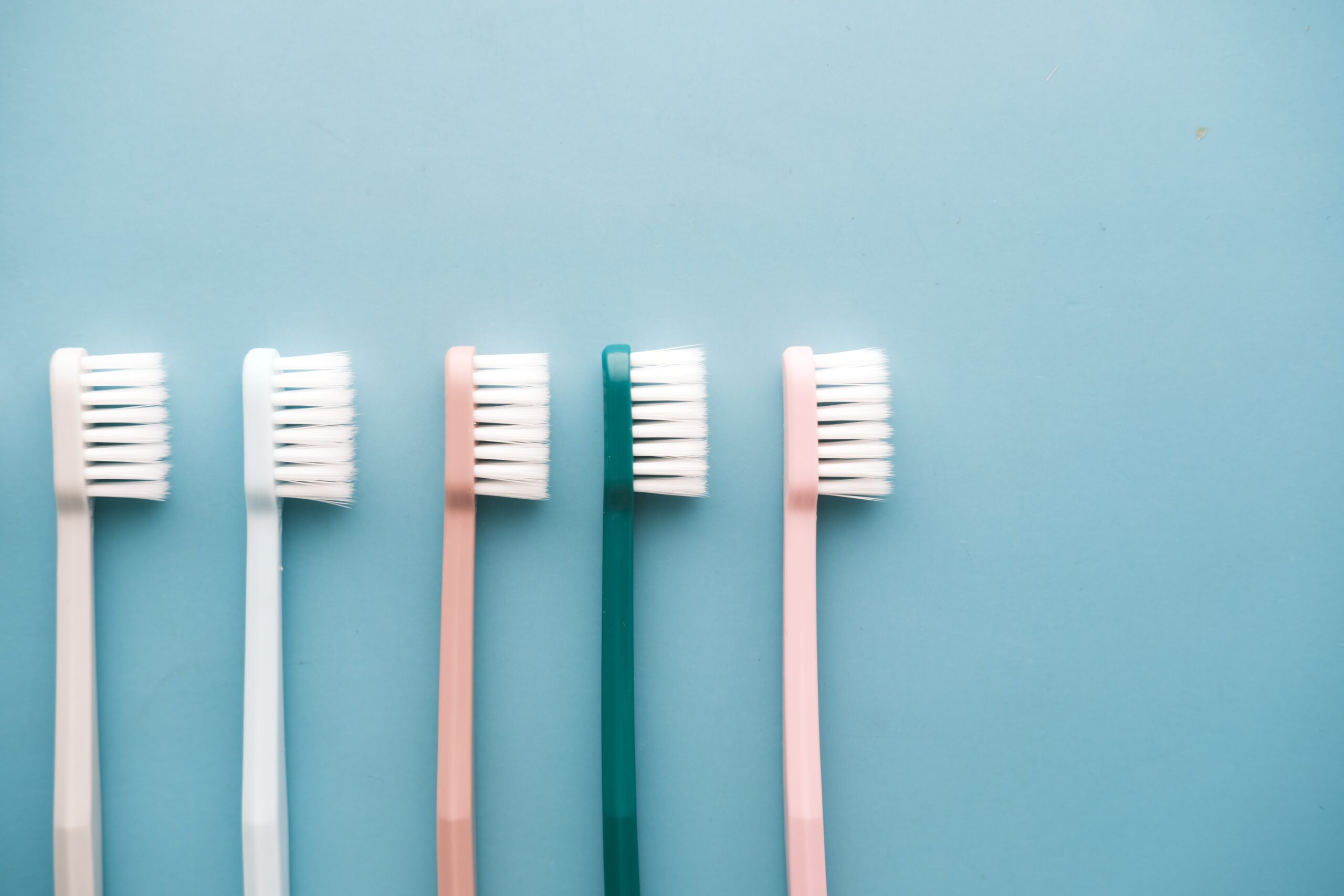 Five toothbrushes with white bristles and differently colored handles