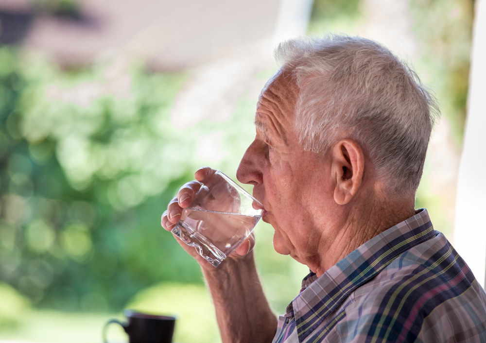 An elderly man drinks a glass of water