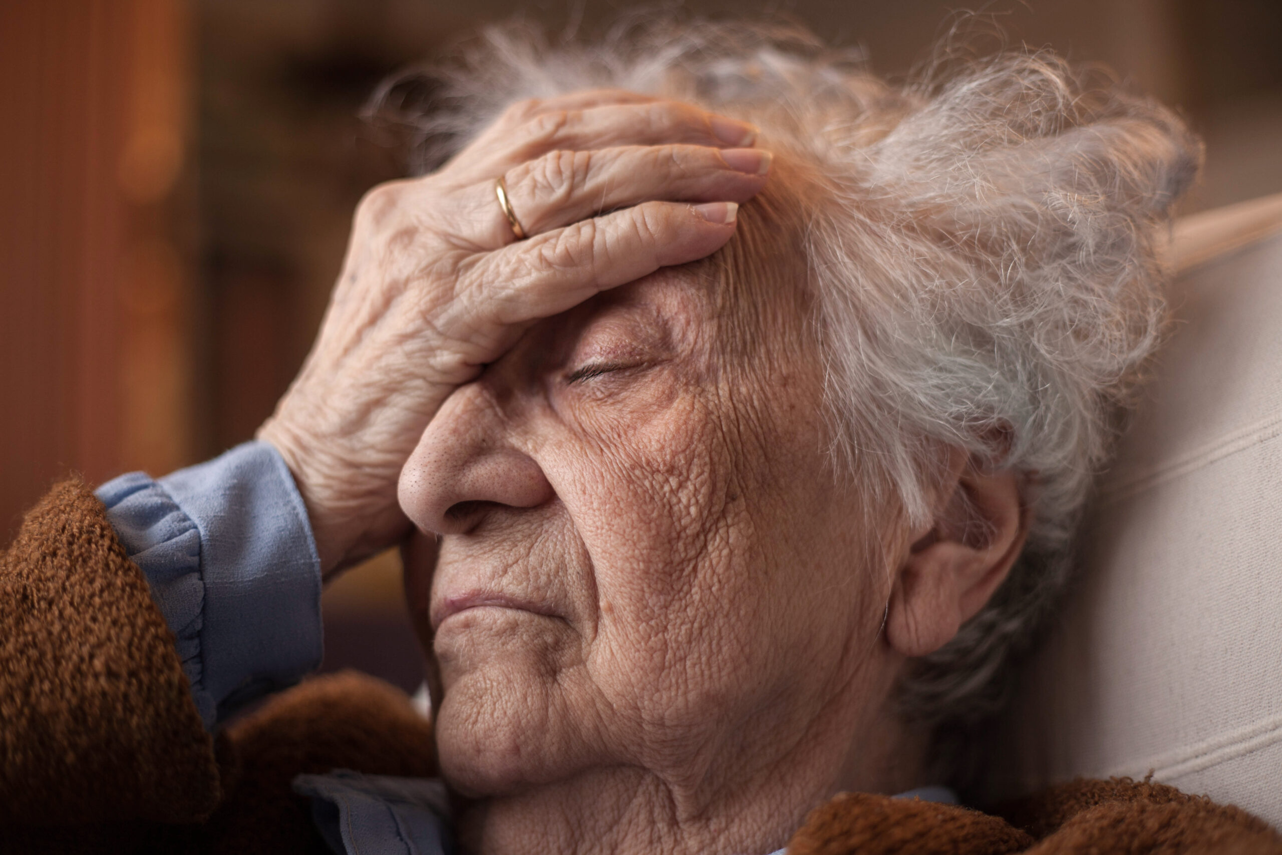 Elderly person with closed eyes and raised hand to forehead