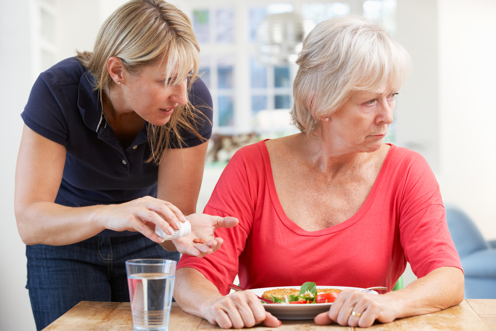 A younger woman offers pills to an older woman who looks away