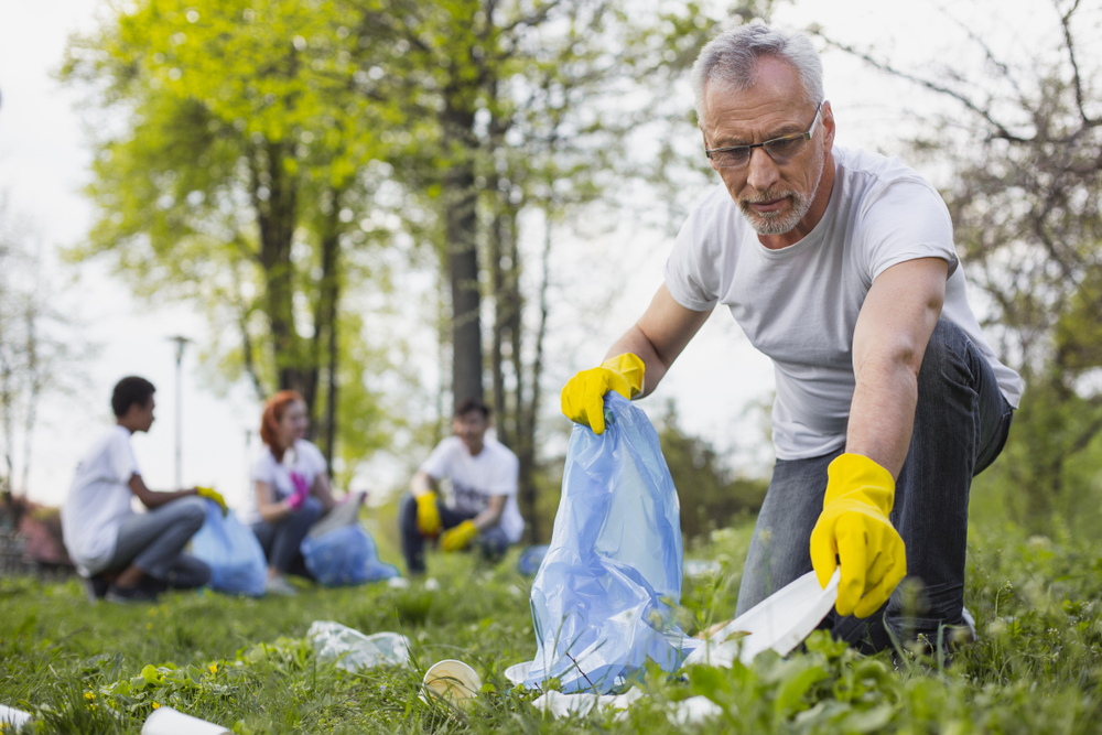 A man wearing yellow gloves picks up trash in a park