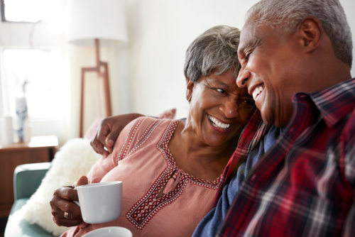 An elderly couple sits closely on a couch