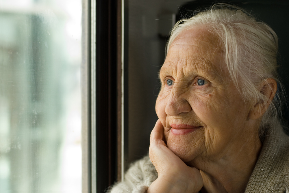 Elderly woman resting her chin on her hand, looking out of a window