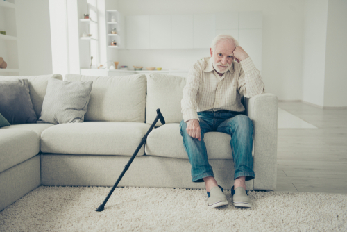 An elderly man sits on a sofa looking pensive