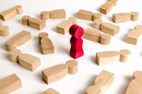 A group of light wooden figures lies scattered with one upright red wooden figure