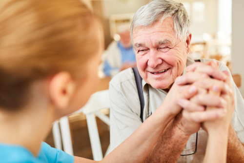 A senior man smiles and holds hands with a younger woman