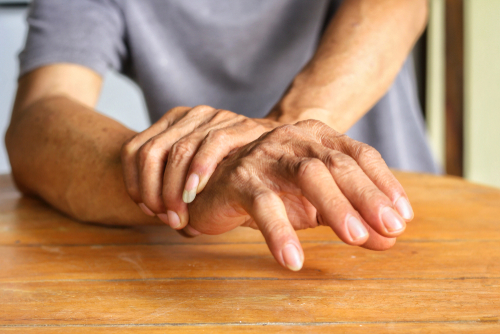 A person places their hands on a wooden table, with the right hand supporting the left wrist