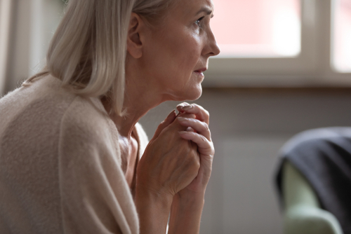 Elderly woman sitting and clasping her hands.