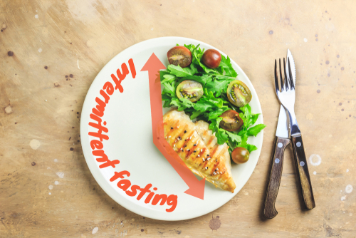 Plate with grilled chicken breast, salad greens, and cherry tomatoes. The text "Intermittent fasting"