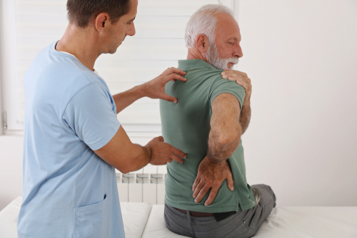 A physical therapist assists an elderly man stretching his back and shoulder