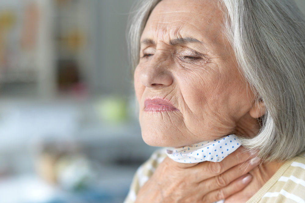 An elderly woman grimacing and touching her throat