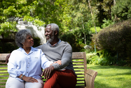 An elderly couple sits on a wooden bench in a garden, enjoying the moment