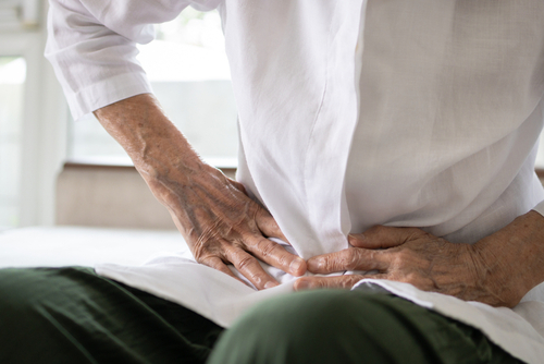 A person in a white shirt, sitting and holding their lower abdomen with both hands