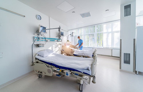 A healthcare worker tends to an empty hospital bed in a clean