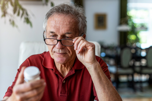 A man adjusts his glasses while reading the label on a bottle