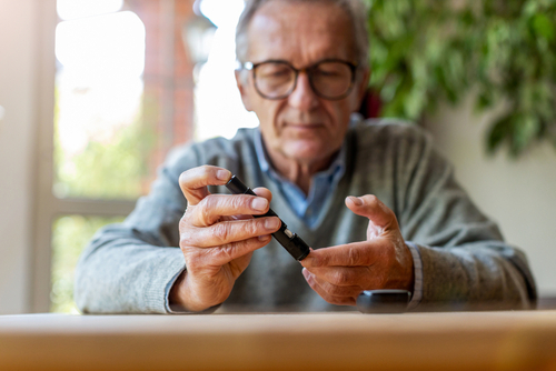 An elderly man holds a diabetes testing device to check his blood sugar levels