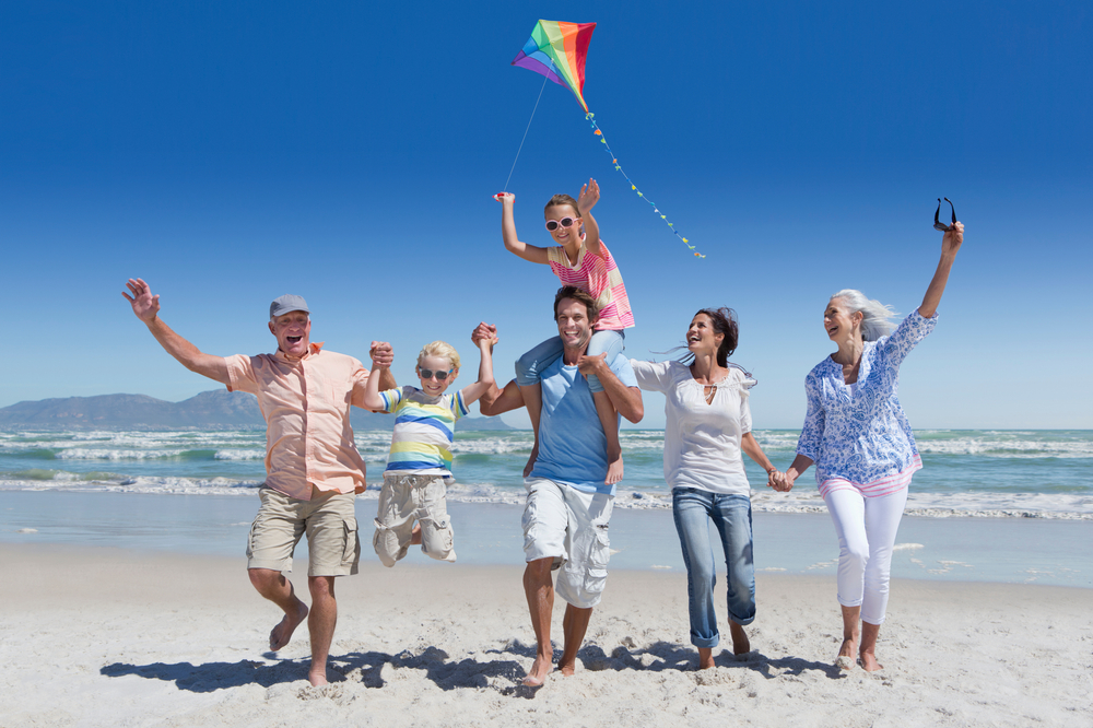 A group of six people, including children and older adults, enjoy a sunny day at the beach