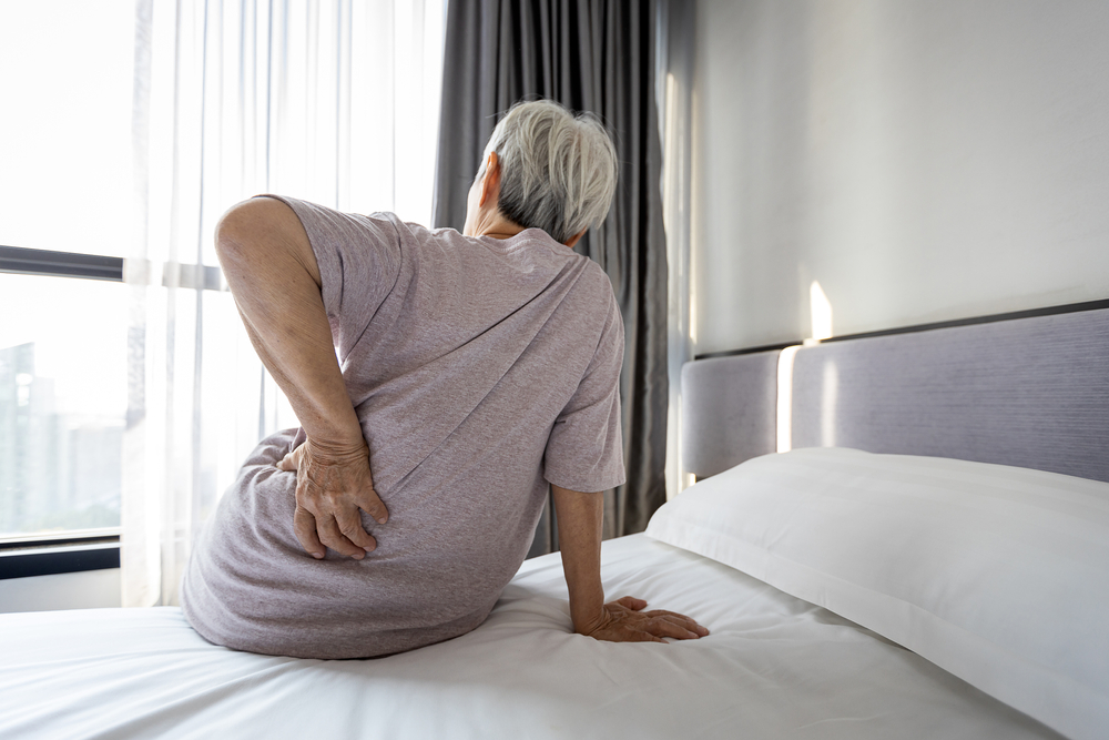 An elderly person holding their lower back