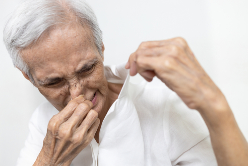 An elderly person holds their nose while pulling the shirt away from their body