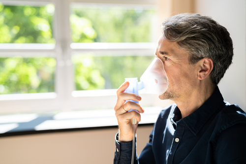 A man uses a nebulizer mask for respiratory treatment while sitting near a window