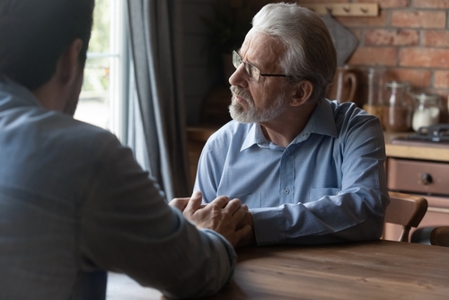 Two individuals are sitting at a table, engaging in a serious conversation