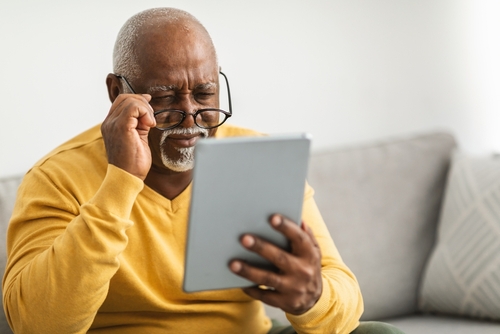 An older man in a yellow sweater is sitting on a couch