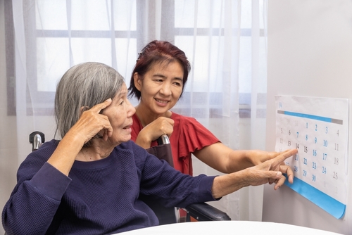 Two women sit together looking and pointing at a wall calendar