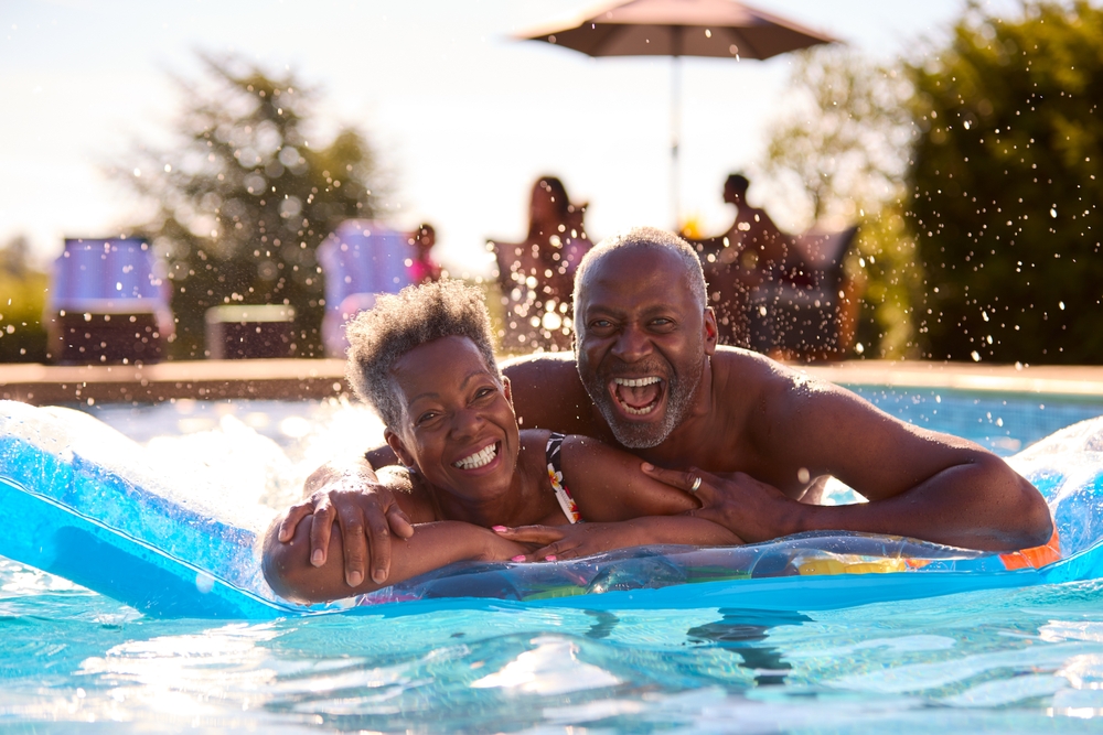 Two adults laugh while lying on a pool float in an outdoor swimming pool