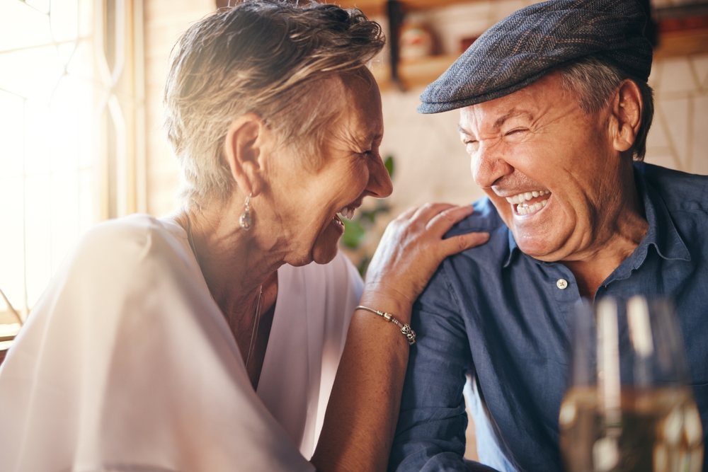 An older couple sits closely together, both laughing heartily.