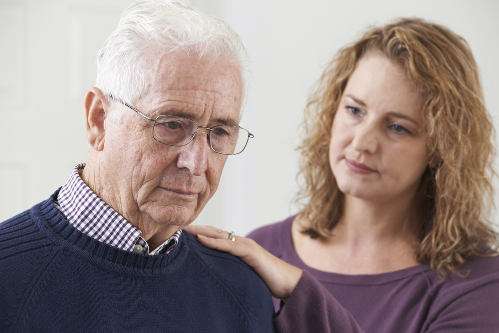 An elderly man looks down pensively