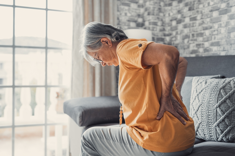 An elderly person holding their lower back with a pained expression