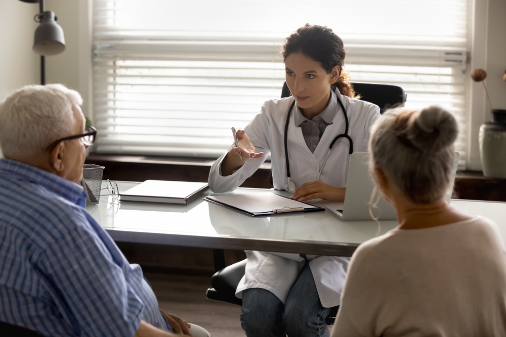 A doctor sitting at a desk, explaining something to an elderly couple sitting opposite her.