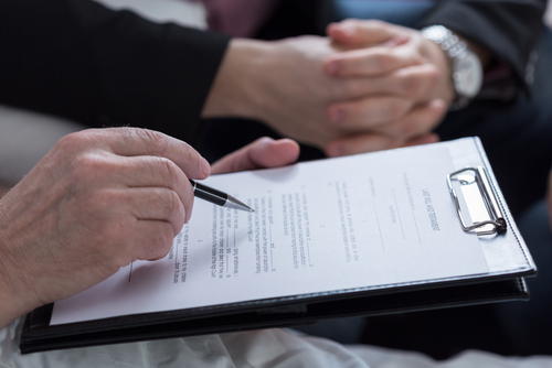 A person holding a pen reviews a document on a clipboard