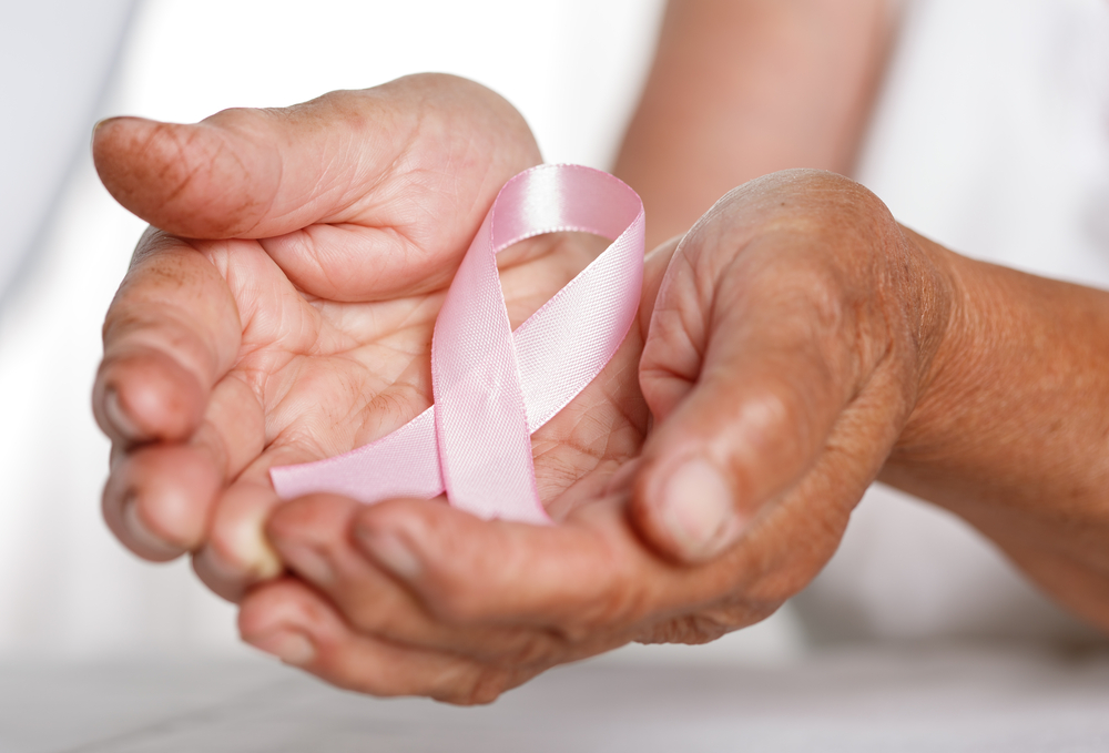 Hands gently holding a pink ribbon, symbolizing breast cancer awareness