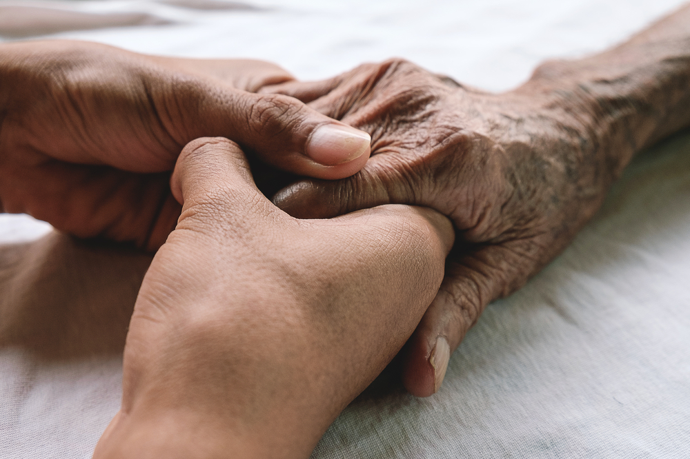 A younger person holds the hand of an older individual