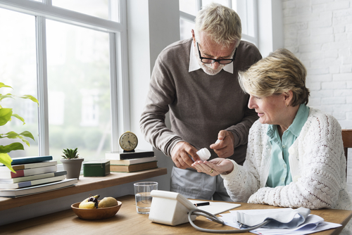 An older man is pouring medication into an older woman's hand