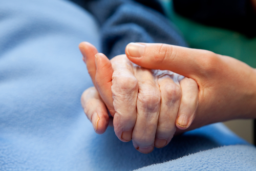 A younger hand gently holds an older hand resting