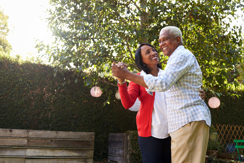 An elderly couple dances outside in a garden