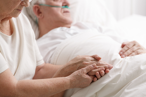 An elderly person wearing an oxygen tube lies in bed