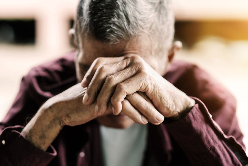 An older person seated, resting their head in their clasped hands