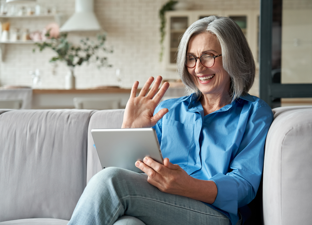 A smiling older woman holding a tablet and waving