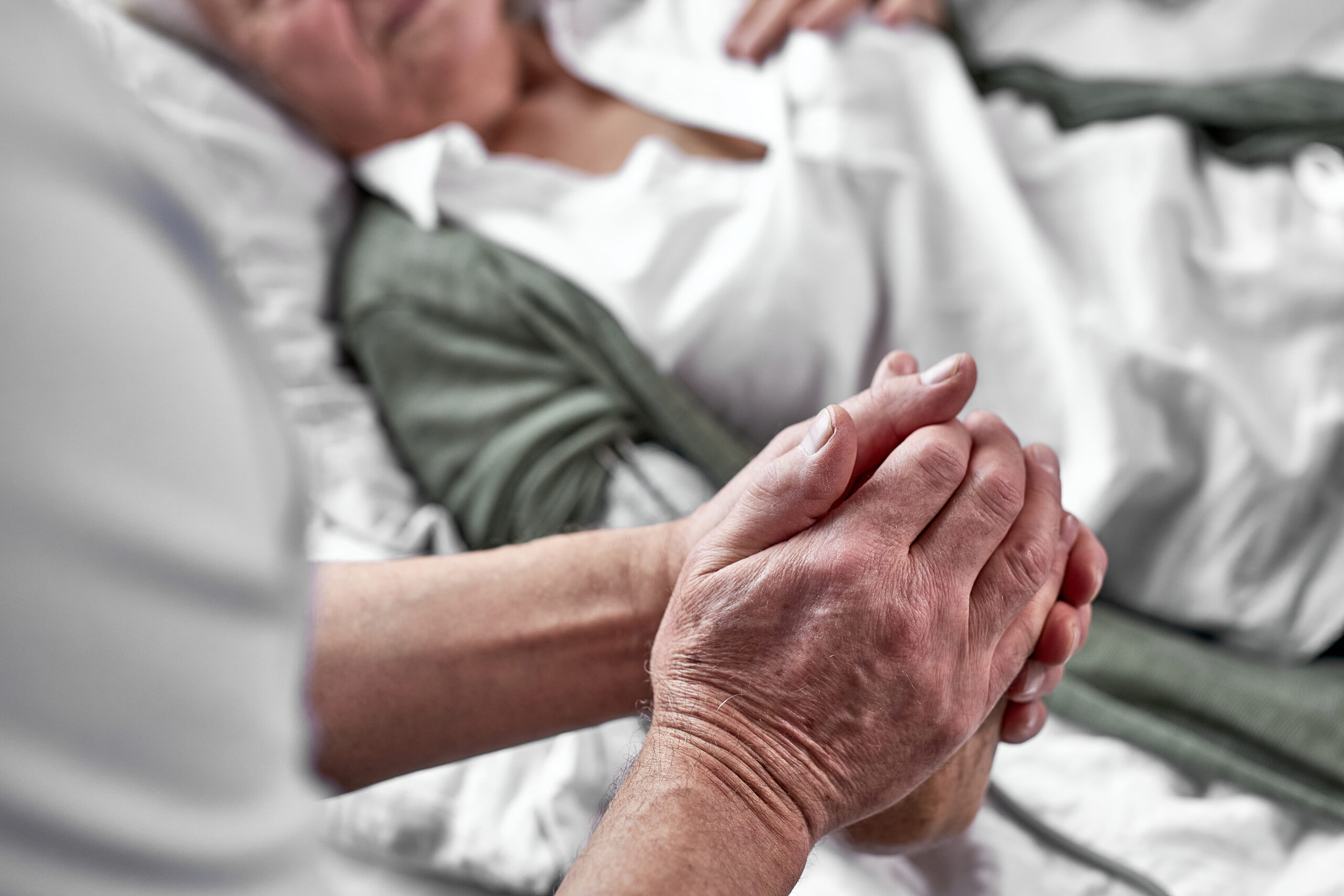 A person holds the hand of an elderly person lying in bed