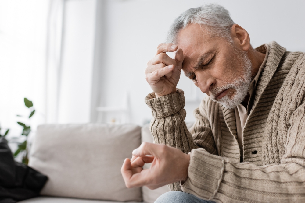 An older man rubs his forehead