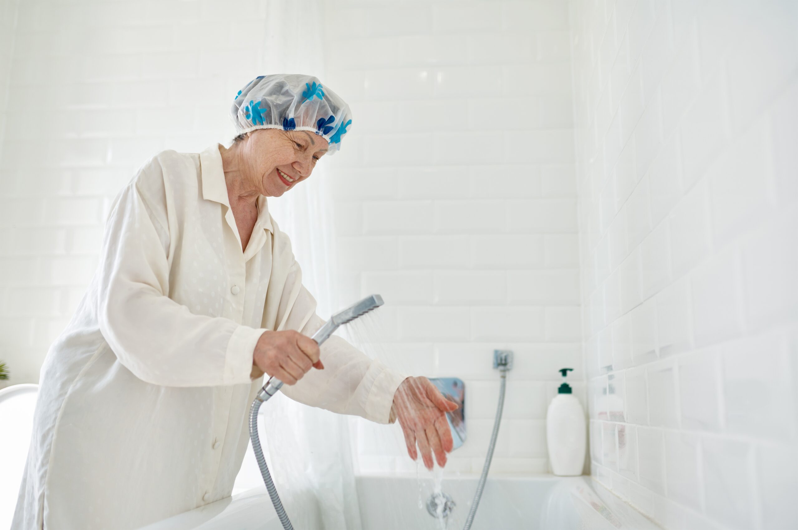 A woman in a shower cap and robe is testing the water temperature