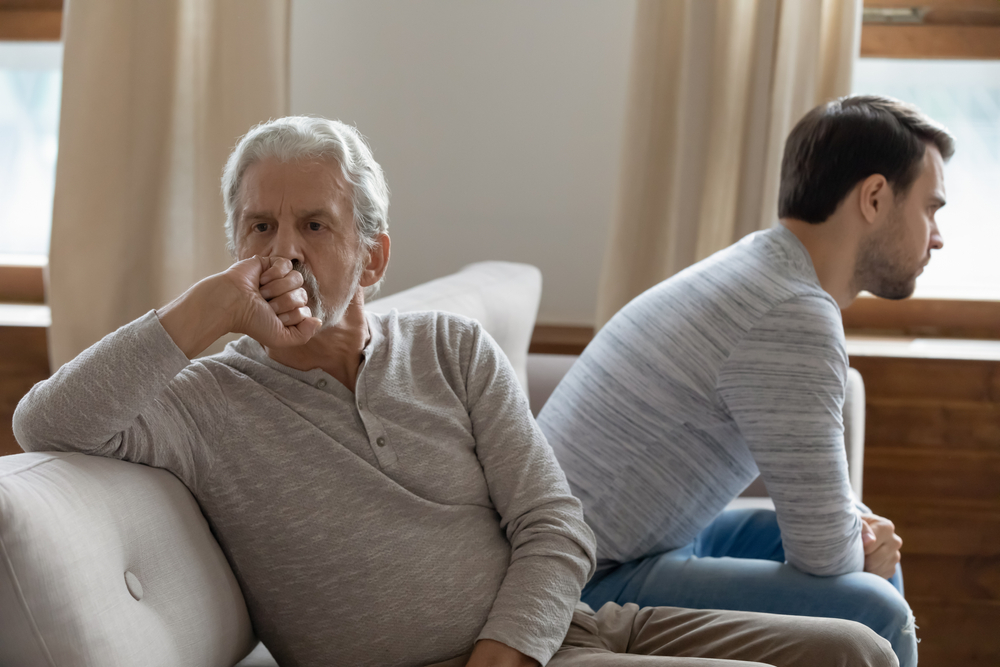 Two men, one older and one younger, sit on a couch facing away from each other