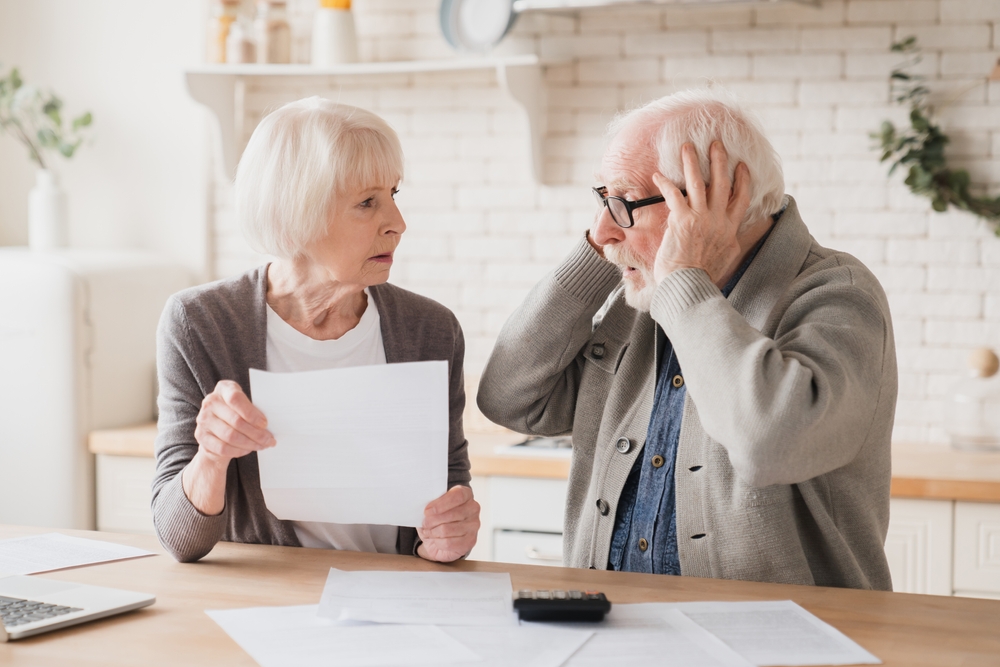 Two elderly people look concerned at financial documents on a table