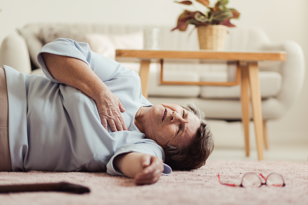 An elderly person lies on the floor holding their chest